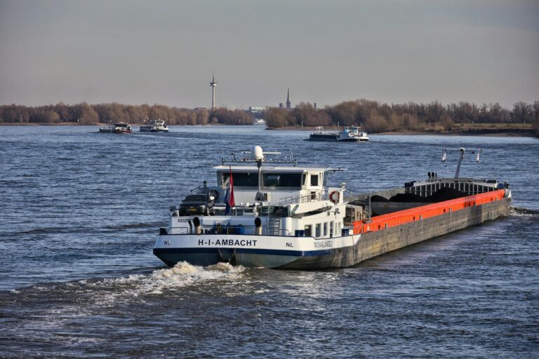 A cargo ship cruising along a wide river under a clear sky, showcasing inland waterway transport.